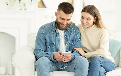 快乐的情侣分享来自智能手机的音乐坐在家里的沙发图片