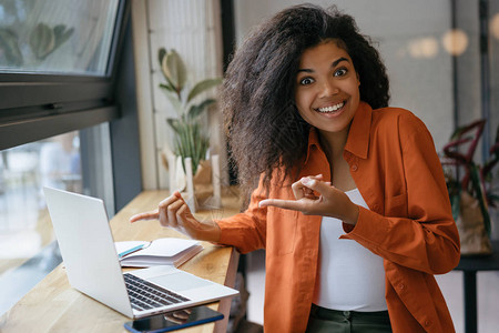 年轻开朗的非洲裔美国女人用两个手指着笔记本电脑屏幕使用笔记本电脑在线购物订购食物订票的情图片
