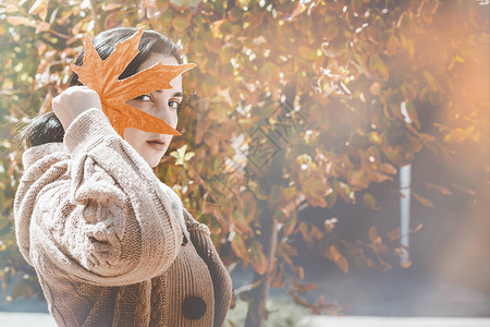 秋分秋季的概念一个美丽的中东女人拿着一片黄色的秋叶年轻女用秋天的树叶遮住她的脸秋天或秋天的女人在户外晴背景