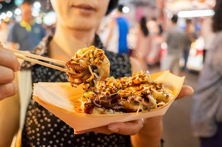 在亚洲的夜市上女人吃著名的天图片