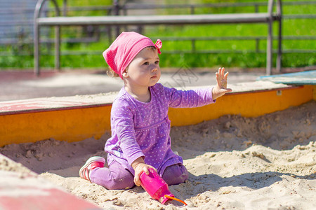 穿着紫色连衣裙的女婴在户外玩具粉红色水壶图片