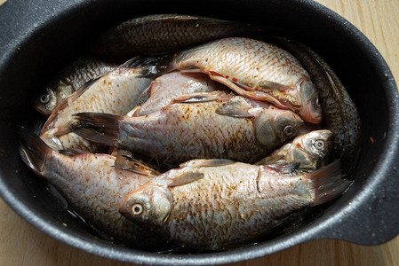 木桌上的圆形铝碗里的鲫鱼河鲫鱼在碗里撒上调味料和盐的鲫鱼就可以在锅里出锅了图片