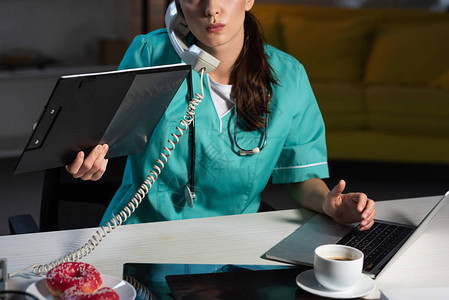 穿制服的护士在夜间值夜班时通过电话交谈并持有剪贴板图片