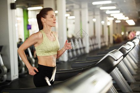 在空体操场复制空间的心胸锻炼期间在跑步机上运行的流汗年轻女背景图片