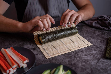 用蟹肉和蔬菜制作自制寿司卷的男人手图片