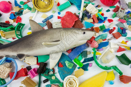 在沙滩上收集的微塑料上的玩具鲨鱼塑料图片