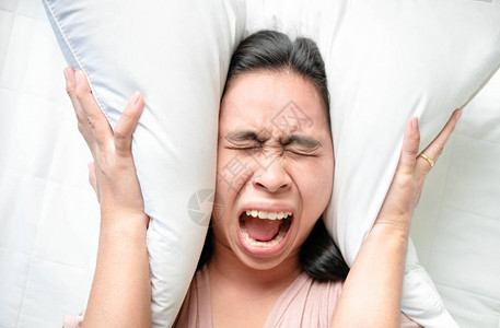 亚洲青年妇女早上在床上用枕头敲响闹钟时图片