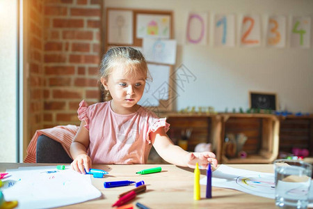 在幼儿园用彩色铅笔绘画的美丽的金发小图片