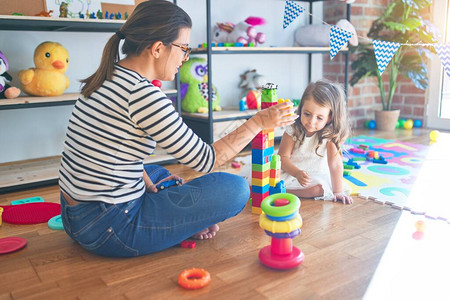 孩子游戏美丽的女教师和幼童在幼儿园里玩许多玩具的建筑砖块背景