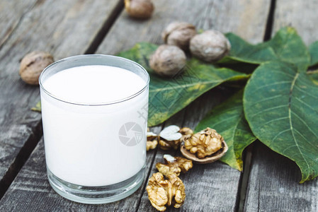 在一张旧木桌上的核桃附近的玻璃杯里放着纯素坚果奶来自核桃的纯素牛奶生态食品图片