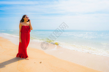 使用手机或手机在沙滩和海上散步的美丽亚洲年轻女肖像图片