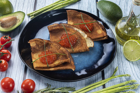 黑色盘子上的红鱼子酱煎饼在木制背景图片