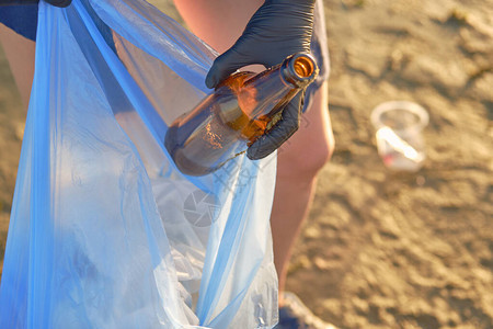 戴着黑手套的年轻女带着垃圾袋沿着河边肮脏的海滩散步图片