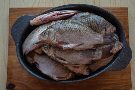 木桌上的圆形铝碗里的鲫鱼河鲫鱼在碗里撒上调味料和盐的鲫鱼就可以在锅里图片