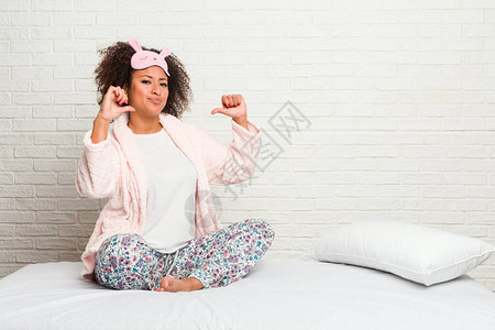 穿着皮雅玛穿衣躺在床上的年轻非洲女感到自豪和自信背景图片