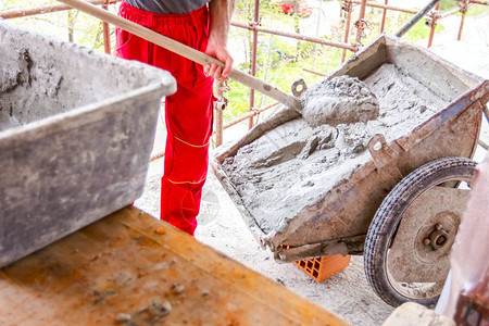 建筑工人正在用铲子从建筑工地的手推车上卸下图片