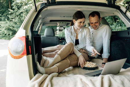 年轻的幸福夫妇穿着白色T恤坐在汽车后备箱里图片