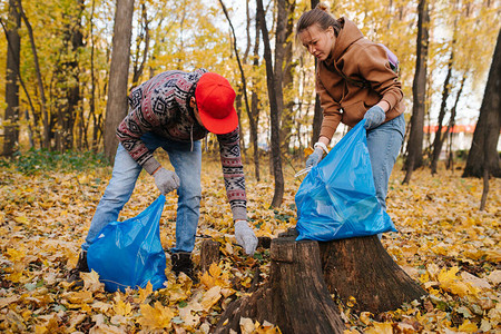 两名中年志愿者带着垃圾袋在季节森林里帮忙打扫图片