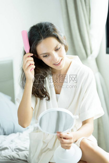 一个穿着毛巾和白色浴袍的漂亮女人必须照镜子用粉红色的梳子理头发图片