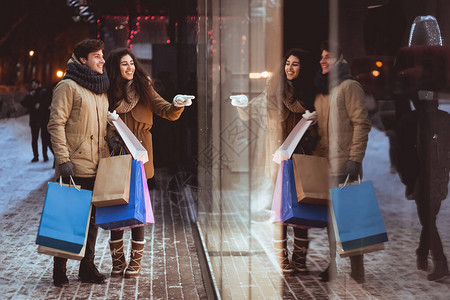 冬季销售部与男朋友一起购物的女孩在夜中走在市内商店窗口图片