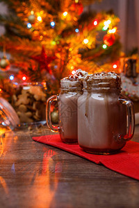 两杯可与生奶油和巧克力糖浆放在木桌和姜饼屋饼干罐和圣诞树上图片