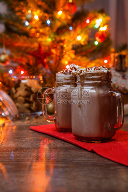 两杯可与生奶油和巧克力糖浆放在木桌和姜饼屋饼干罐和圣诞树上图片