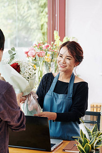 穿着蓝色围裙的漂亮花店家给顾图片