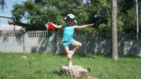 一个戴着儿童巴拿马帽的小女孩单腿站在公园的树桩上孩子手里拿图片