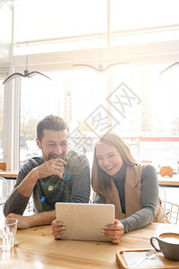 年轻快乐的一对夫妇在咖啡馆看线上触摸器视频时笑着图片