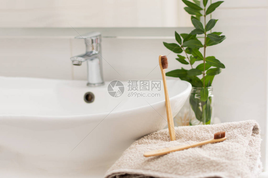 浴室白色内饰的毛巾上放着两把棕色可生物降解可堆肥的竹牙刷背景中的图片
