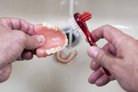 用自来水和牙刷清洁和清洗水槽中的假牙图片