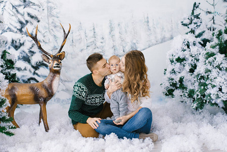 年轻父母与婴儿坐在冬季照片区的人造雪中图片