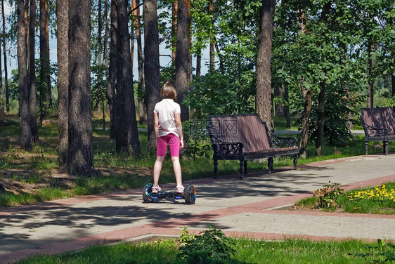 一个女孩骑着一辆自制平衡的摩托车沿着树丛之图片