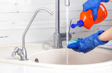 戴蓝色手套的女人把洗涤剂倒在海绵上洗碗背景图片