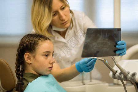 女牙医对坐在牙科诊所牙科诊疗椅上的一名小女病人进行X光图片