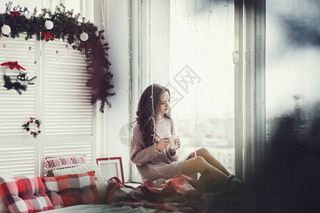 女人坐在窗台上在圣诞节日喝热茶或咖啡图片