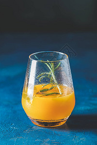 深蓝色混凝土背景的玻璃杯中加入橘子和迷迭香的黄橙色鸡尾酒图片