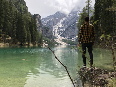 在白天森林覆盖的山中站在湖岸边的男旅行图片