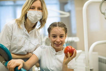 女牙医在现代牙科诊所为微笑的少女赠送苹图片