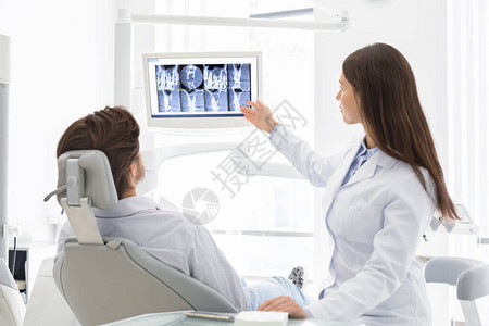 女牙医生解释其病人坐在椅子X光检查结果的图片