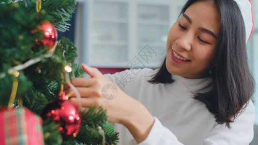 亚洲妇女在圣诞节装饰圣诞树女青少年快乐地微笑着在家里的客厅里庆祝圣诞节的寒背景图片