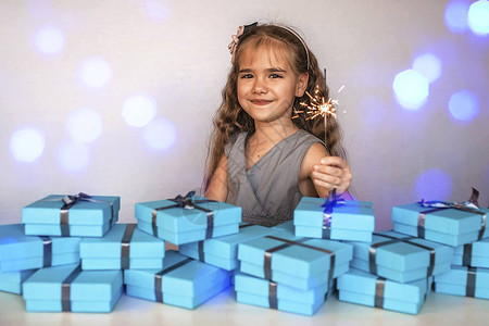 可爱的小女孩与烟花闪光灯在一大批蓝色礼物箱附近灰色丝带隔离在白色图片