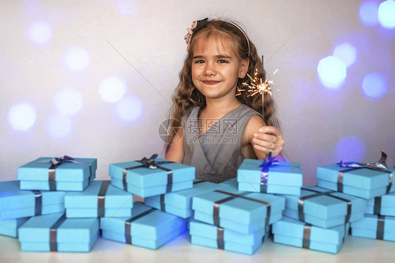可爱的小女孩与烟花闪光灯在一大批蓝色礼物箱附近灰色丝带隔离在白色图片