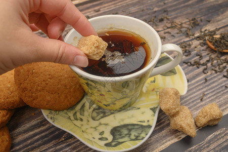 女孩的手把一块棕色糖放进一杯黑茶燕麦饼干茶叶图片