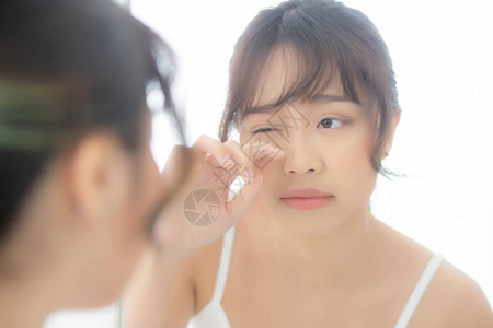 美丽和化妆年轻的亚洲女在脸上和触摸眼睛上看着镜子老化图片
