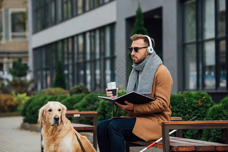 盲人耳机持书的盲人和导盲狗旁图片