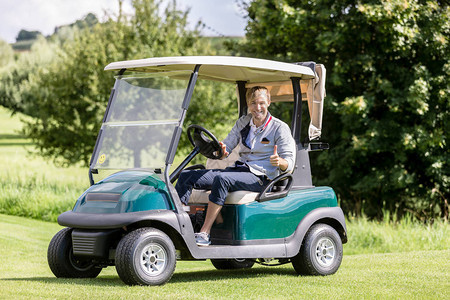微笑的男高尔夫球手骑着高尔夫球车显示拇指标志的肖像图片