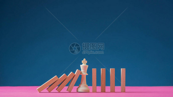 王象棋站在多米诺落地的中间防止他们完全倒塌在海军蓝色背景和复制空间图片