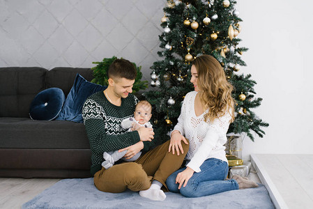 年轻快乐的父母和他们的小儿子在家中的圣诞树上庆祝图片