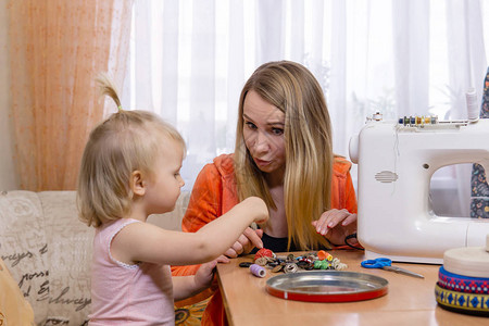 裁缝妇女中断在家的工作与女儿一起玩图片